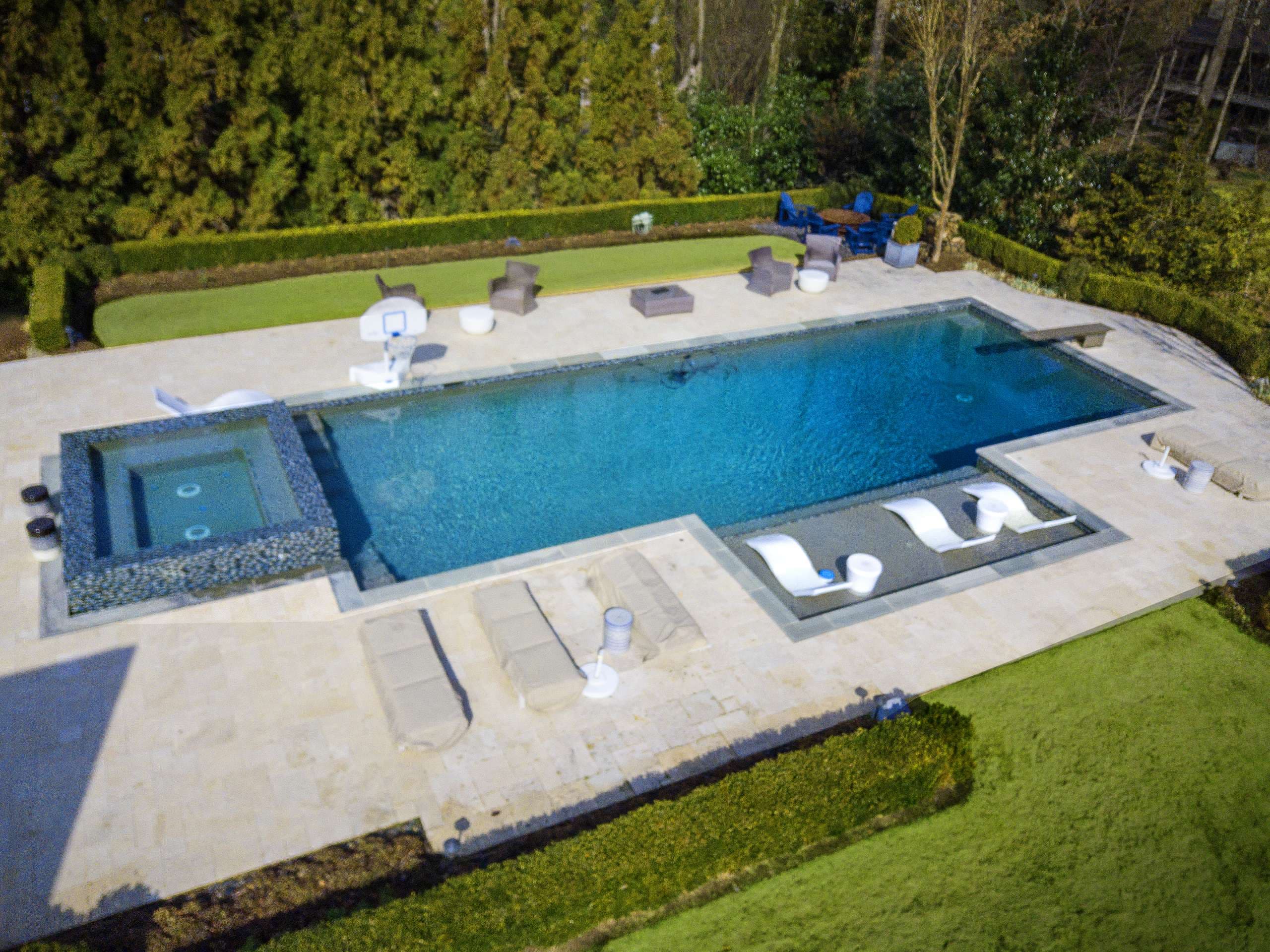 Pool with travertine deck, tanning ledge, spillover spa, and basketball hoop
