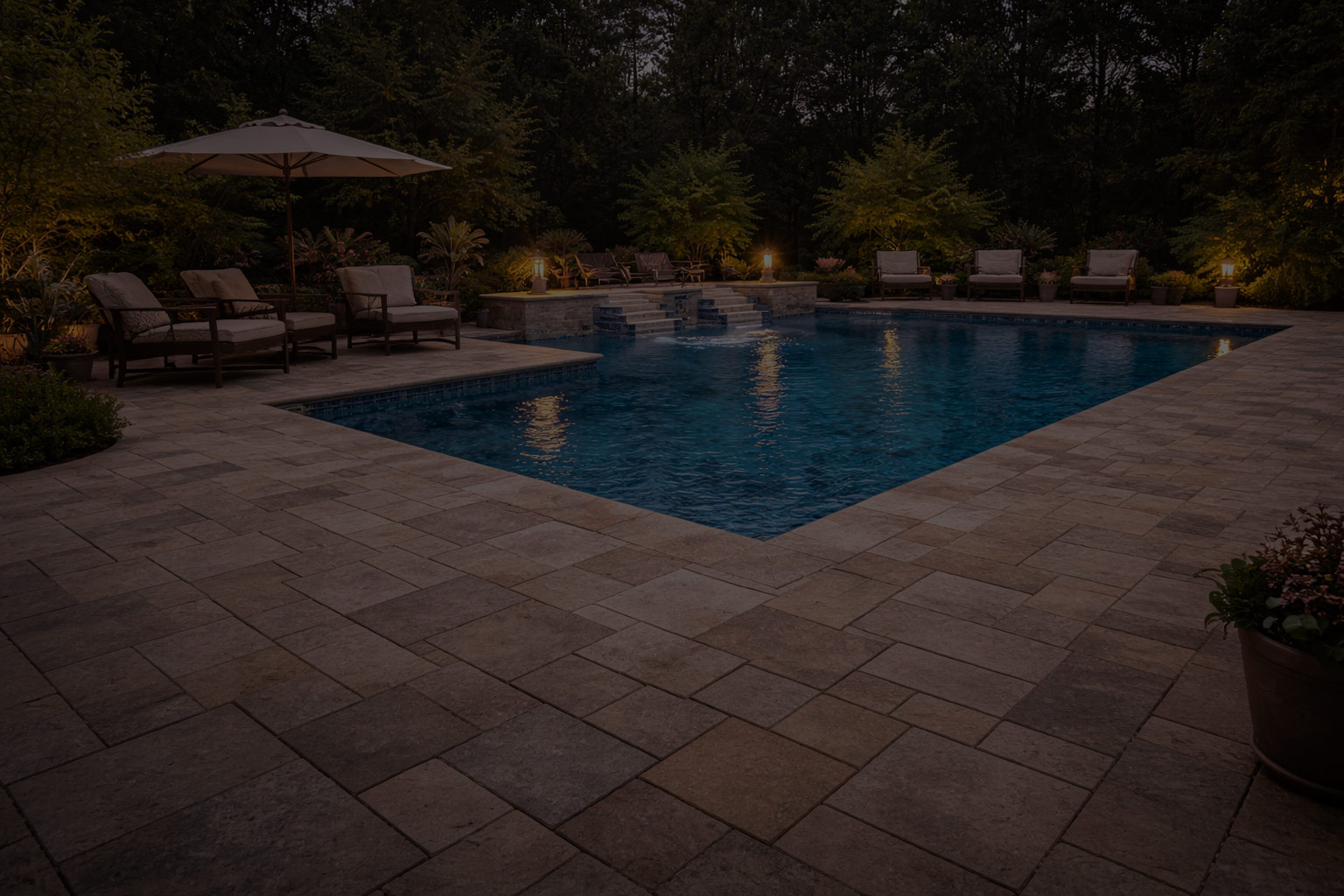 Pool deck with natural stone pavers illuminated at dusk